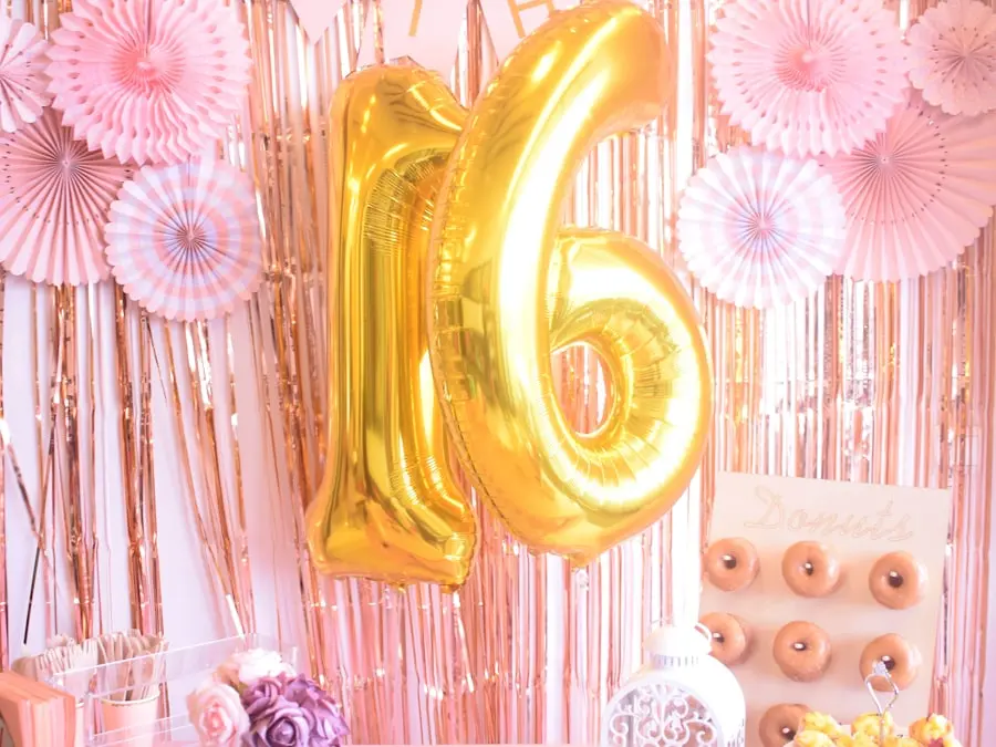 A styled milestone birthday backdrop with gold number balloons and a donut wall